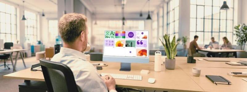 מבט אחורי על אדם במשרד מודרני, העובד על מחשב iMac המציג בבירור ערכת מיתוג גרפית בולטת